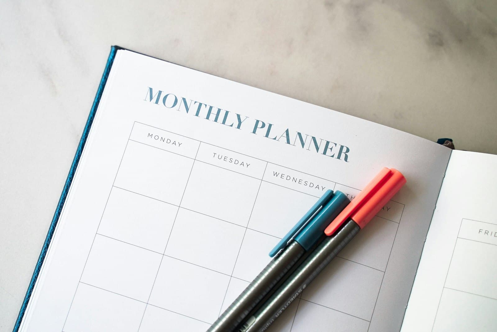 An open monthly planner with two pens resting on it