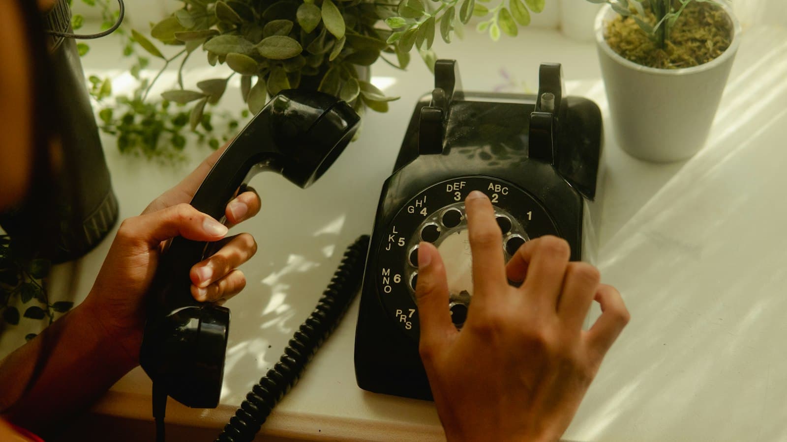 A hand dialling a black rotary telephone on a desk