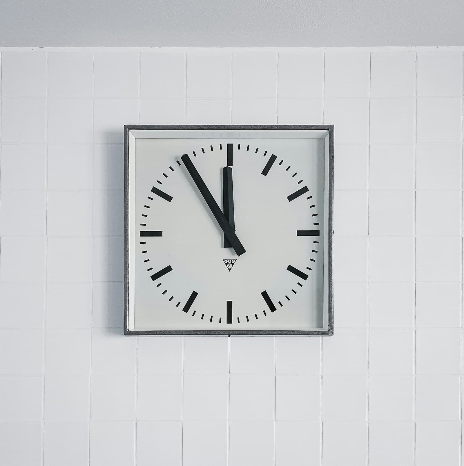 A square wall clock on a white tiled wall
